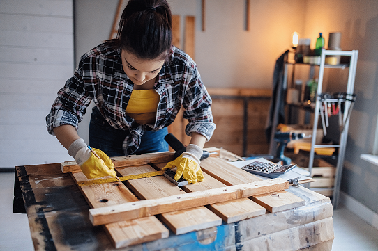 A woman works on a wood carpentry project in a home garage.