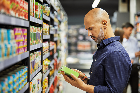 A man reads the label on a product in a supermarket aisle.